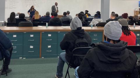 A classroom of high school students sit in a classroom while representatives from the Cook County Public Defender's Office speak at the front of the room. 